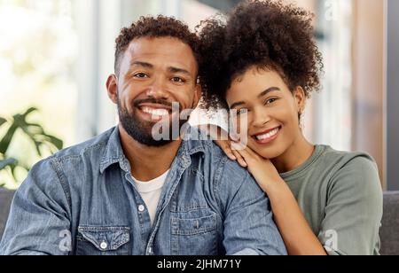 Ritratto di una felice coppia mista di gara sorridente mentre si rilassa insieme a casa. Spensierate il marito e la moglie ispanici che si legano insieme nel salotto di Foto Stock