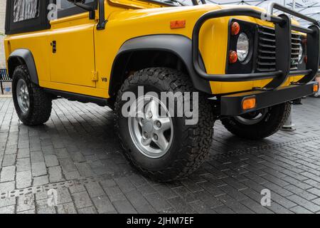 Un frammento di jeep gialla con una ruota anteriore e un paraurti in piedi sul marciapiede Foto Stock