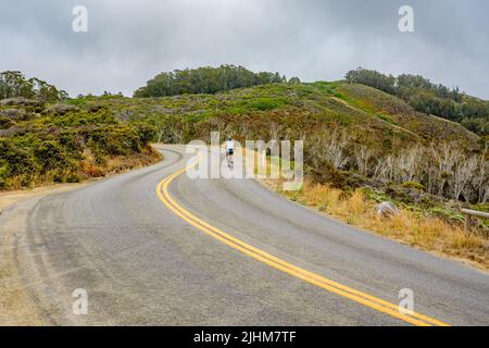 Curving asphalt road with yellow lines, and silhouette of bicyclist, serpentine way Foto Stock