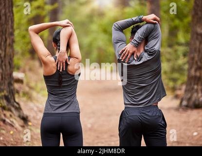 Vista posteriore del giovane atleta maschile e femminile che si allunga prima di una corsa all'aperto in natura. Due sportivi in forma che fanno esercizi di riscaldamento nella pineta su un Foto Stock