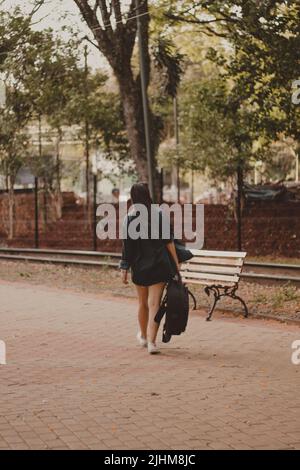 giovane donna che cammina verso la panchina con la sua chitarra sulla schiena Foto Stock