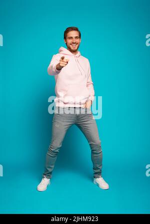 Foto a grandezza naturale di uomo bruna sorridente puntando il dito sulla fotocamera isolata su sfondo azzurro Foto Stock