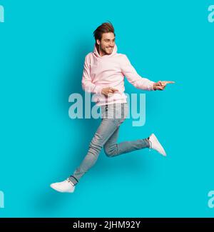 Foto a grandezza naturale di giovane felice eccitato sorridente positivo uomo che salta isolato su sfondo di colore azzurro chiaro Foto Stock