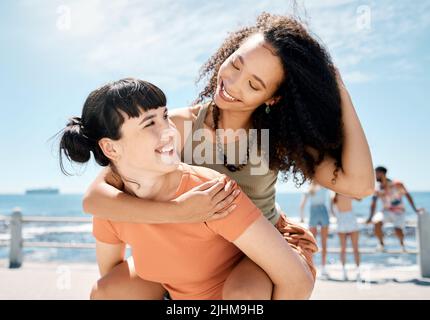Ci piace la vita ogni minuto di risveglio. Una giovane donna attraente che le dà un'amica un giro di piggyback mentre si unisce all'esterno. Foto Stock