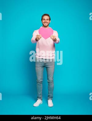 Sia la mia ragazza. Ti voglio bene. Ritratto di tenero romantico dolce dolce dolce grazioso uomo a cuore aperto che mostra grande cuore rosso in mani isolate su azzurro b Foto Stock