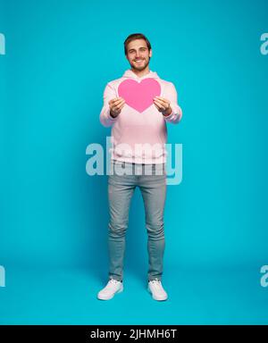 Sia la mia ragazza. Ti voglio bene. Ritratto di tenero romantico dolce dolce dolce grazioso uomo a cuore aperto che mostra grande cuore rosso in mani isolate su azzurro b Foto Stock