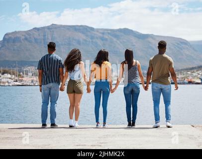 I veri amici non sono mai separati. Ripresa retrostensiva di un gruppo di amici che tengono le mani mentre si alza insieme su un molo. Foto Stock