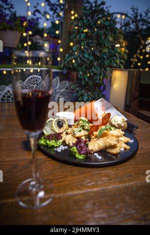 antipasto in pastella con patate su un piatto nero con vino. Foto Stock