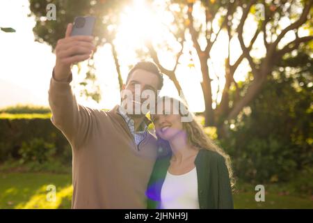 Immagine di felice coppia caucasica che prende selfie in giardino Foto Stock