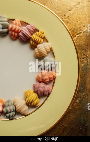 Conchiglie a conchiglia di mare colorate 'Conchiglioni' disposizione di pasta in cerchio su piatto giallo dorato con spazio copia al centro Foto Stock