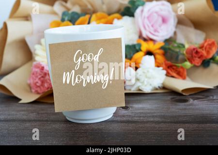 Buona mattina saluto su nota adesiva con tazza di caffè e fiore Foto Stock