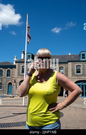 Donna matura turista che indossa occhiali da sole e un top giallo su un telefono cellulare durante le vacanze in estate. Foto Stock