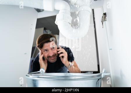 Uomo preoccupato che chiama idraulico mentre osserva l'acqua che perde da Sink Foto Stock