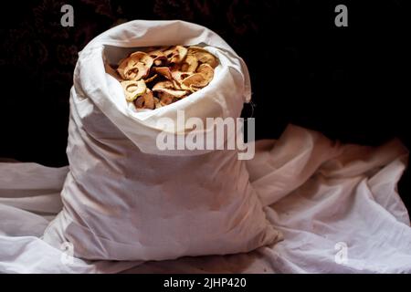 Mele secche in anelli in un sacchetto bianco su sfondo scuro. Scorte per l'inverno. Uno spuntino sano con vitamine Foto Stock