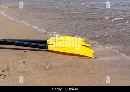Pagaia gialla in kayak sulla spiaggia di ciottoli. Attrezzatura sportiva per kayak. Foto Stock