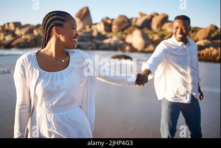 Una giovane coppia amorevole che ha un momento romantico mentre tiene le mani e balla o si segue mentre la moglie si porta in spiaggia. Felice Foto Stock