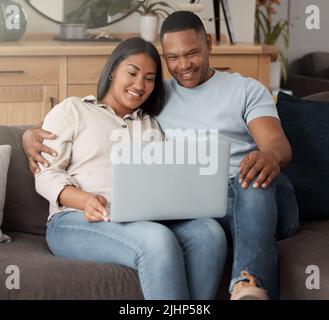 Bella coppia giovane gara mista rilassarsi sul divano e utilizzando un computer portatile. Sorridente coppia afroamericana che guarda i film mentre è affettuoso Foto Stock