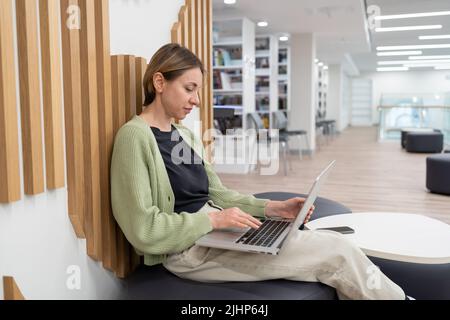 Autore freelance focalizzato donna che lavora su un notebook in biblioteca. Freelance dopo il 40 Foto Stock