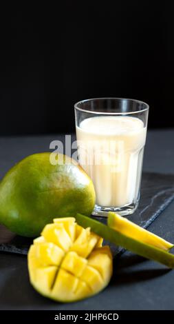 Bevanda al latte su sfondo nero con mango. Un classico milkshake di mango - Lassi. Una bevanda tradizionale in India dal calore Foto Stock