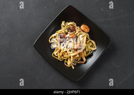 Piatto tradizionale italiano e romano, fettuccini con spinaci e funghi su un piatto nero su sfondo scuro sottostante. Pasta romana. Superiore Foto Stock