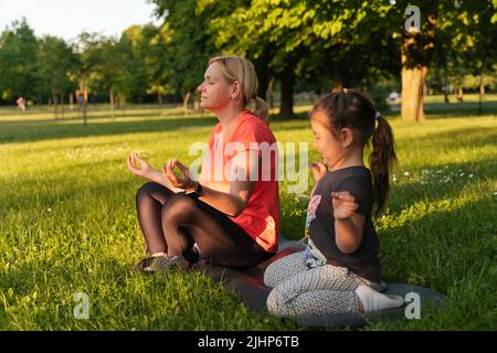 Madre di mezza età con bambino meditare insieme nel parco Foto Stock