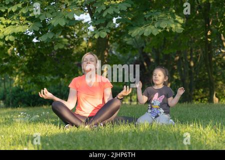 Madre di mezza età con bambino meditare insieme nel parco Foto Stock