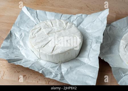 Due teste di formaggio Camembert su carta bianca su tagliere. Preparazione per la cottura alla griglia Foto Stock