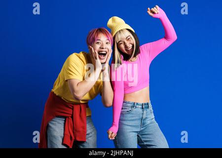 Coppia asiatica con i capelli multicolore ridendo e ballando insieme isolato su parete blu Foto Stock