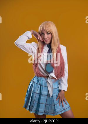 Affascinante giovane modella femminile in camicia bianca e gonna con capelli rosa guardando la fotocamera mentre si trova su sfondo marrone in studio chiaro Foto Stock