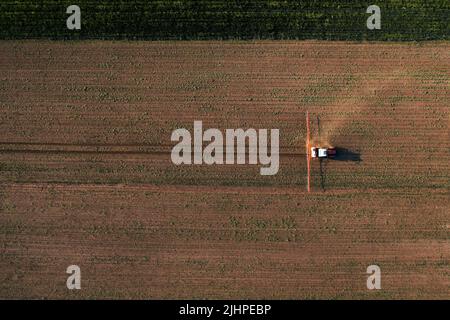 Colpo aereo del trattore agricolo con irroratrice montata spruzzando erbicida chimico sopra piantagione di mais, drone pov direttamente sopra Foto Stock