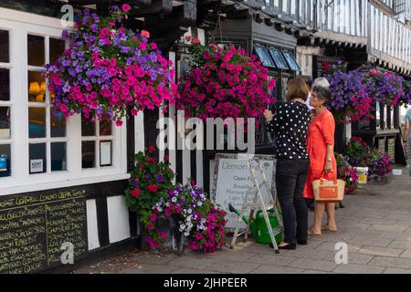 Una donna nutre cesti appesi con acqua in un caldo giorno d'estate fuori dal caffè di alberi di limone, tenterden, kent, uk Foto Stock