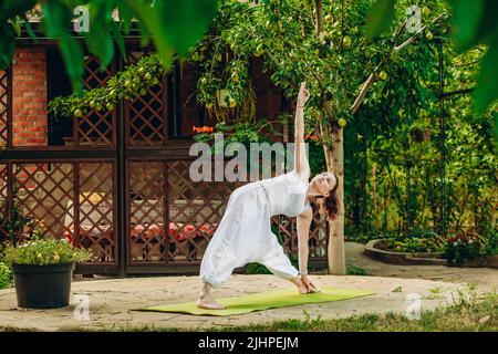 Donna pratica yoga nel giardino estivo: Utthita Trikonasana, allungata posa Triangolo. Foto Stock