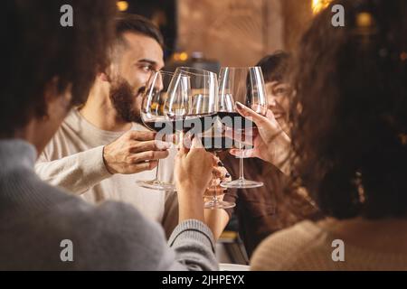 Gruppo di giovani amici che brinda con vino rosso per festeggiare al ristorante - giovani adulti che si aggraffano alzando i vini - gente amicizia e vita Foto Stock