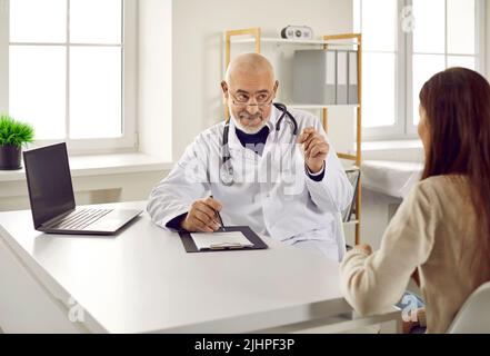 Il medico maschile senior consiglia la paziente sulla sua diagnosi mentre si siede in ufficio della clinica medica. Foto Stock