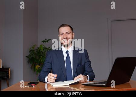 Felice uomo d'affari seduto e utilizzando un computer portatile al coperto Foto Stock