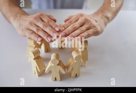 Uomo che copre figure umane in legno come il manager aziendale che protegge il team di dipendenti Foto Stock