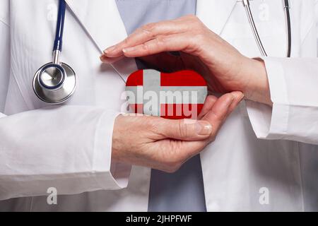 Medico danese che tiene il cuore con bandiera di sfondo Danimarca. Concetto di assistenza sanitaria, beneficenza, assicurazione e medicina Foto Stock