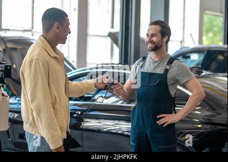 Meccanico che prende la chiave dell'auto dall'uomo con pelle scura Foto Stock