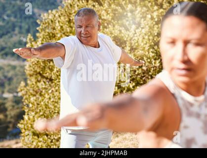 Anziani che vivono uno stile di vita sano ed esercitarsi all'aperto. Coppia anziana in piedi in posizione di guerriero mentre pratica yoga in natura in una giornata di sole Foto Stock