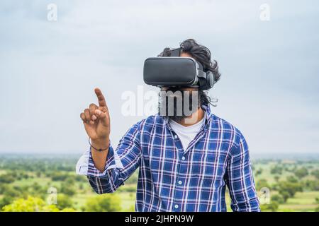 Giovane uomo di barba che utilizza la realtà virtuale in cima alla collina toccando i gesti delle mani sulla natura: Concetto di interazione virtuale, innovazione e intrattenimento. Foto Stock