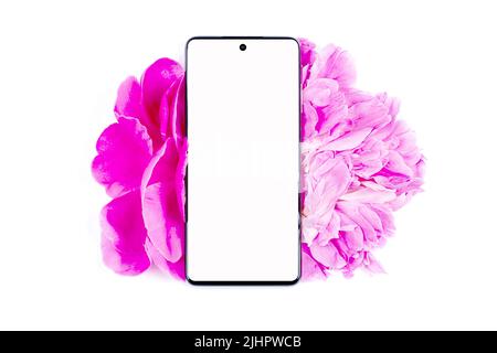 Il telefono è in fiori rosa e petali di peonia su sfondo bianco. Mock-up Foto Stock