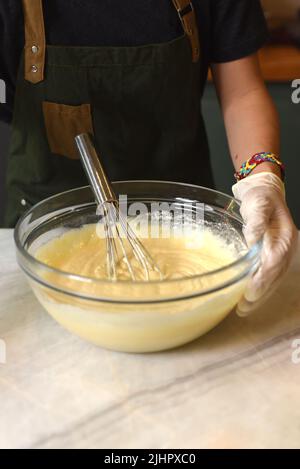 Una mano in guanto di gomma mescolando l'impasto per una torta Foto Stock