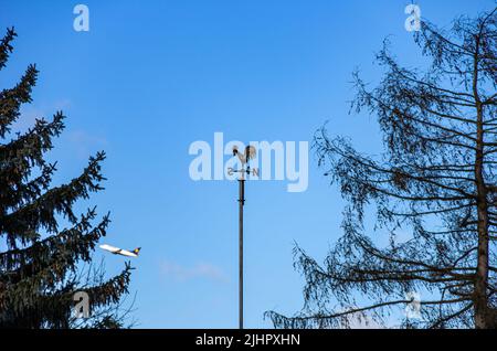 Paletta meteo o rubinetto con indicatore di direzione del vento sotto forma di una rosa bussola e due cime di mezzo albero, mentre un getto decola sullo sfondo. Foto Stock