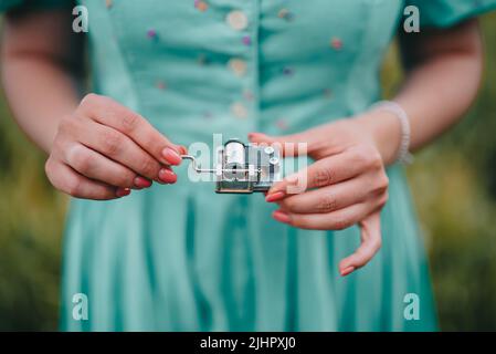 Le mani femminili ruotano gli ingranaggi del vecchio meccanismo della scatola musicale. Lady girando leva di retro piccolo carillon metallico. Donna in abito d'epoca che ascolta musica Foto Stock