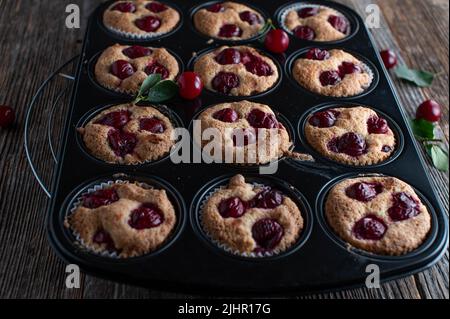 Muffin alle ciliegie appena sfornati e fatti in casa in una teglia isolata su un tavolo di legno. Primo piano Foto Stock