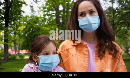 madre e figlia in maschere mediche blu nel parco Foto Stock