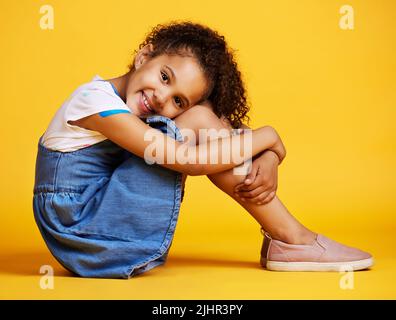 Studio ritratto misto razza ragazza guardando seduto da solo isolato su uno sfondo giallo. Carino ispanico bambino in posa all'interno. Ragazzo felice e carino Foto Stock