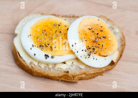 piccolo panino aperto con uova sode e pepe nero su tavola di legno primo piano selettivo Foto Stock