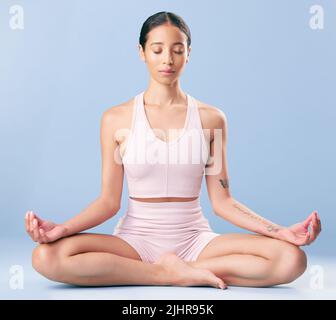 Gara mista fitness donna meditando e praticando yoga in studio su uno sfondo blu. Giovane ispanica femmina trovare il suo centro, la pace interiore e. Foto Stock