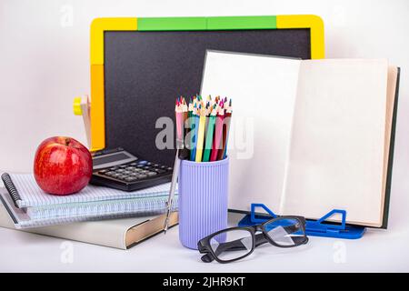 Vado a scuola presto. Lavagna, cancelleria, libro aperto e ramo di lilla bianca su sfondo ligneo Foto Stock